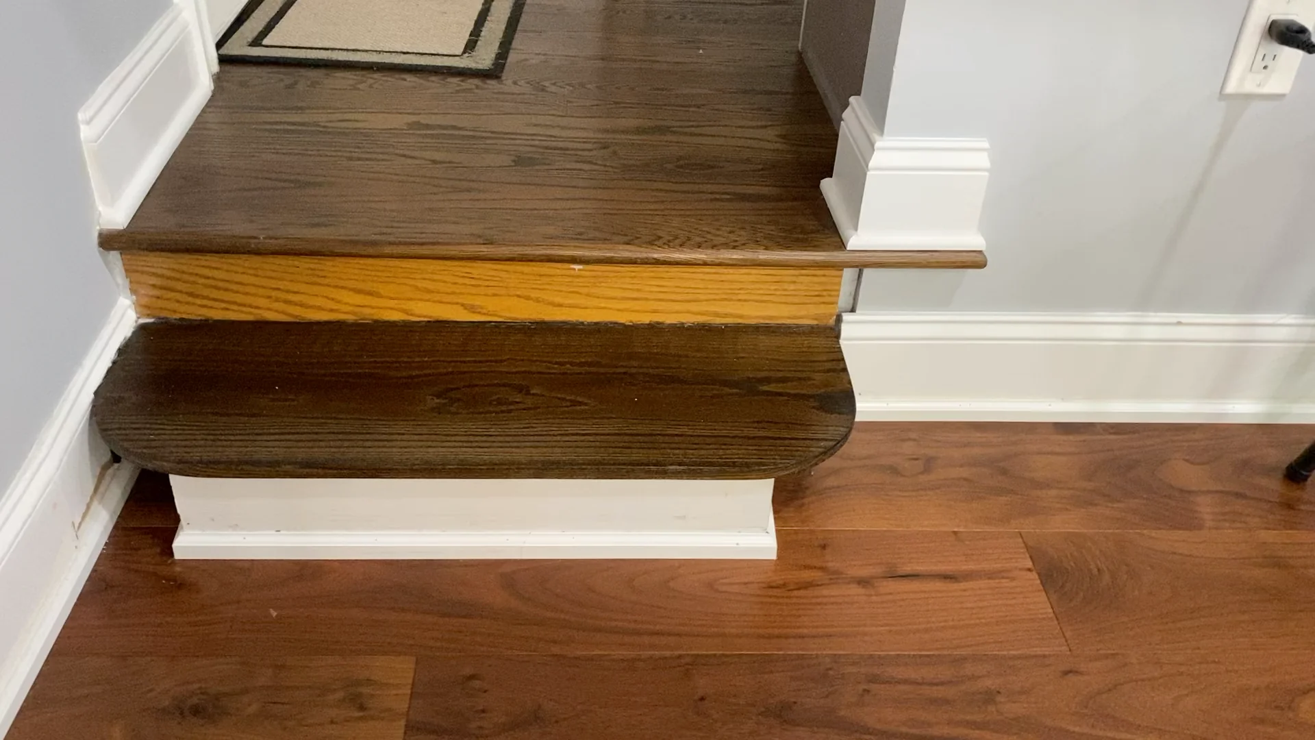 Close-up view of a stair step intersection with contrasting stained wood against the newly refinished hardwood floor, depicting the detail and care taken in a project. The image reflects the expert refinishing work that enhances the wood's natural texture and color in a residential setting.